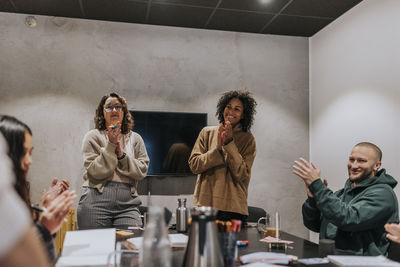 Smiling multiracial male and female colleagues applauding in meeting at startup company