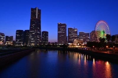 Illuminated minato mirai by bay against sky