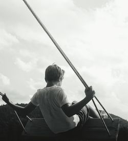 Rear view of boy swinging against sky