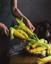 Midsection of person holding sweetcorn at home