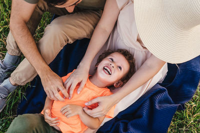 Directly above shot of parents tickling son on blanket in park