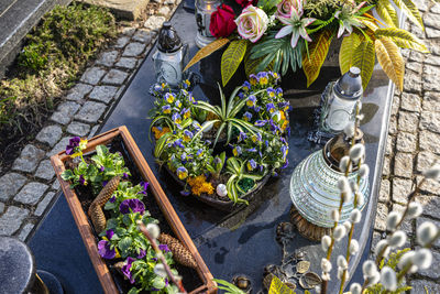 Purple pansy flowers and spruce cone in a heart-shaped pot standing on a tombstone in  cemetery.