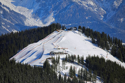 Far sunny hill with snow, evergreen forest and ski camping among winter alps of austria