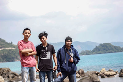 Portrait of friends standing on shore against sky