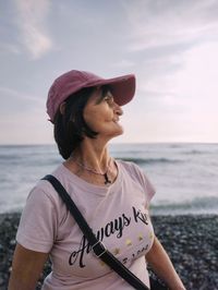 Young woman wearing hat standing at beach against sky during sunset