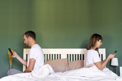 Young man using mobile phone while sitting on bed