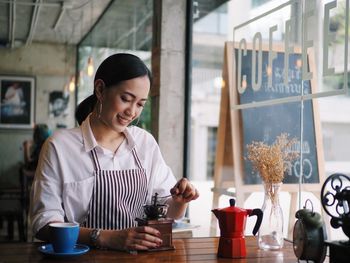 Smiling young woman standing by coffee in cafe