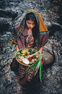 High angle view of woman carrying fruits in basket while standing in river