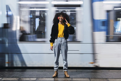 Smiling young woman standing in front of moving tram at night