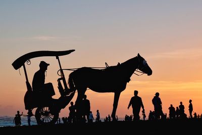 Silhouette people riding horses against sky during sunset