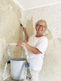 Portrait of smiling young woman standing against wall at home