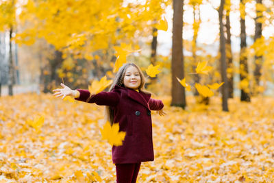 Dreamy cute little girl in autumn clothes in a park with yellow leaves. a smiling child is playing