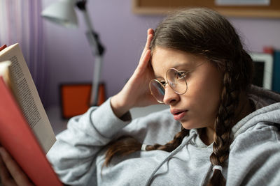 A teenage girl with glasses reads her next school reading with interest.