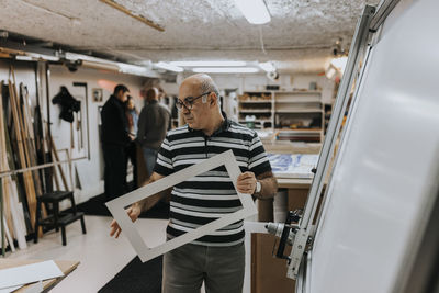 Senior male entrepreneur wearing eyeglasses examining frame in workshop