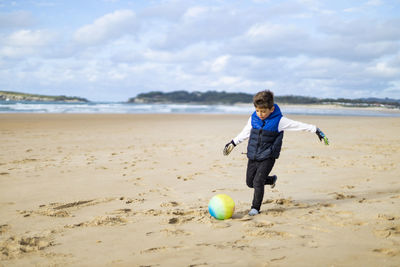 Cute boy playing with ball at shore of beach