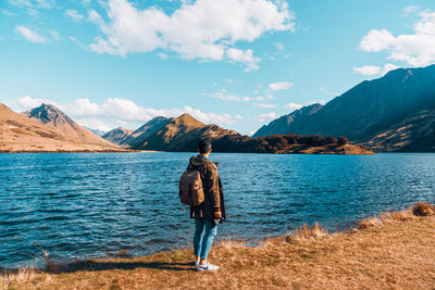 Rear view of man standing by lake against sky