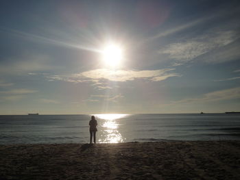 Silhouette woman standing on beach against bright sun