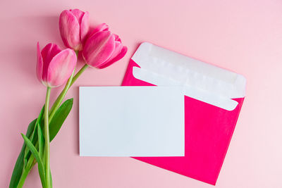 Envelope with invitation to holiday and bouquet of tulips on pink background. place for text.