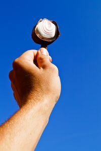 Cropped hand holding ice cream against clear blue sky