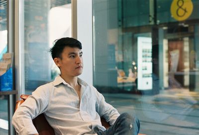 Mid adult man looking away while sitting on chair by window