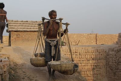 Man carrying baskets while walking on land against clear sky