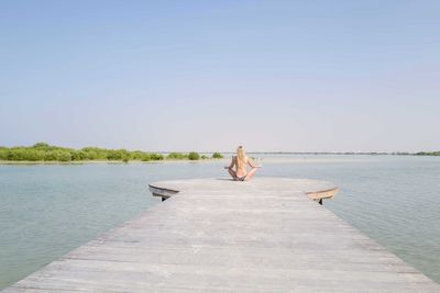 Rear view of woman walking on pier over lake against clear sky