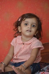 Portrait of cute girl sitting against red wall