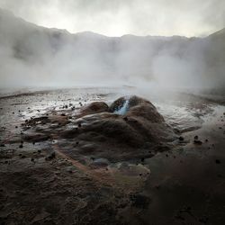 Geyser emitting by mountains against sky