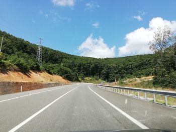 Empty road by trees against sky