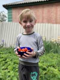 Portrait of smiling boy holding strawberries standing outdoors