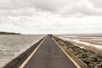 Man walking on road amidst sea against sky