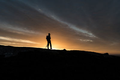 Silhouette man standing on field against sky during sunset