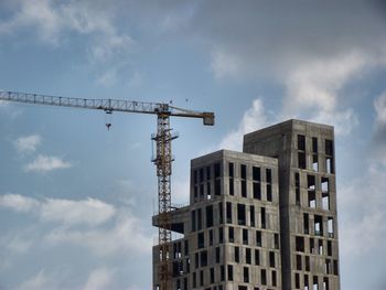 Low angle view of crane by building against sky