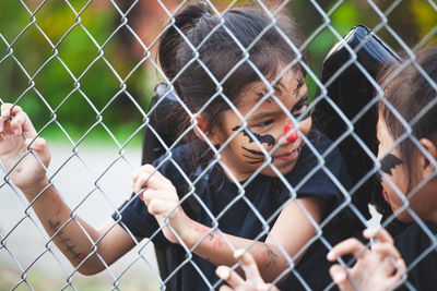 Close-up of friends wearing halloween costumes standing by chainlink fence