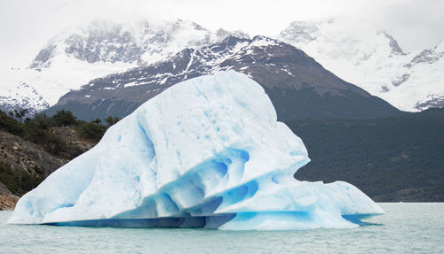 Scenic view iceberg against snowcapped mountains in the background.