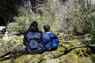 Back view of two young teenagers sitting on river shore