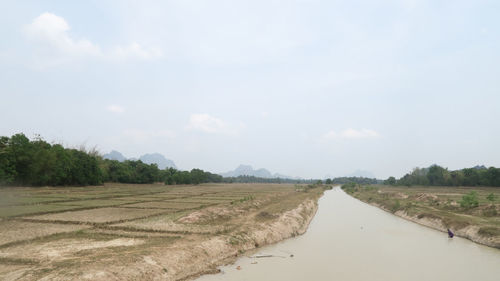 Empty road amidst field against sky