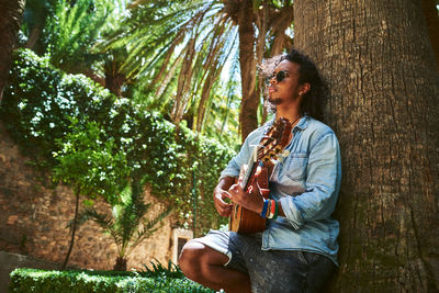 Young woman playing guitar on tree trunk