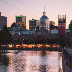 River by illuminated buildings against sky at dusk