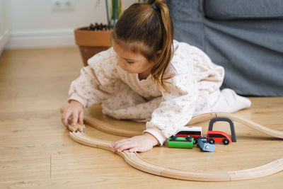 Toddler girl in white dress plays with wooden train at home in the living room