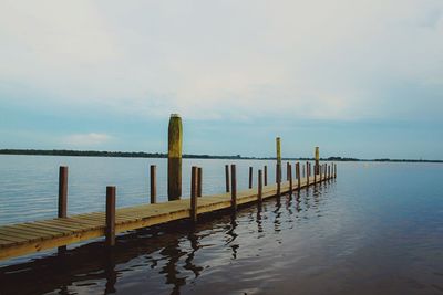 Wooden posts on pier over sea against sky