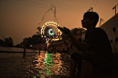 Silhouette boy splashing water at river at night