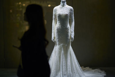 Silhouette woman standing by mannequins in wedding dress at bridal shop