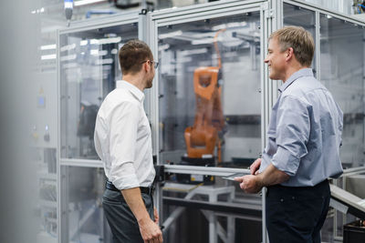 Two businessmen having a meeting at industrial robot in a factory