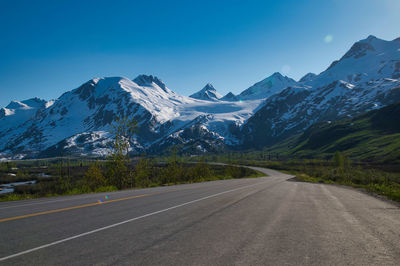 Road by snowcapped mountains against sky