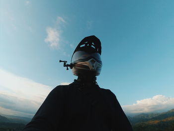 Low angle view of man wearing helmet standing against sky