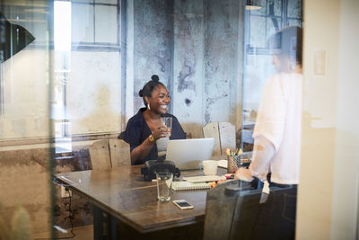 Creative businesswoman smiling while holding glass during meeting with colleague in office