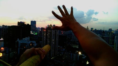 Midsection of man holding cityscape against sky during sunset