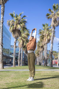 Full length of woman exercising while standing on grass against sky