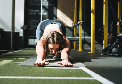 Young brunette woman doing stretching pilates, practice yoga on mat in fitness club gym